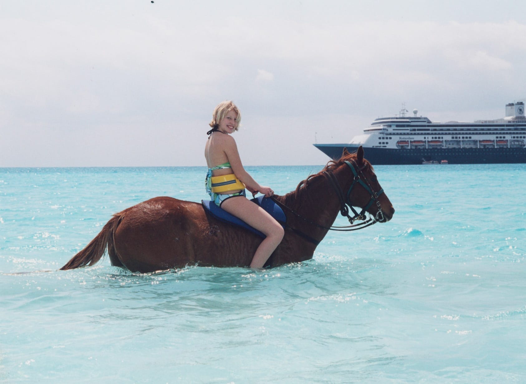 Person wearing a swimsuit and life jacket rides a horse